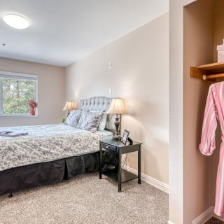 A cozy bedroom with a large bed, side tables with lamps, and an open closet displaying a pink robe.
