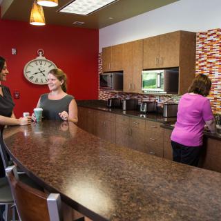 Three people interacting in an office kitchen area.