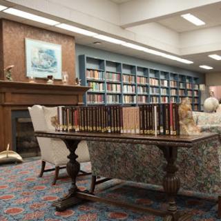 A cozy library setting featuring a table, comfortable chairs, and a well-stocked bookshelf.
