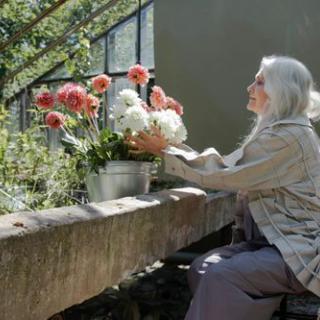 An elderly woman lovingly arranges a bouquet of flowers in a serene garden setting.