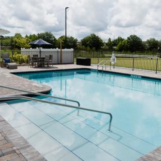 An outdoor swimming pool with patio furniture and a fence under an overcast sky.