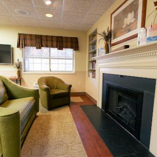 A cozy living room featuring a green chair, a fireplace, and shelves adorned with decorative items.