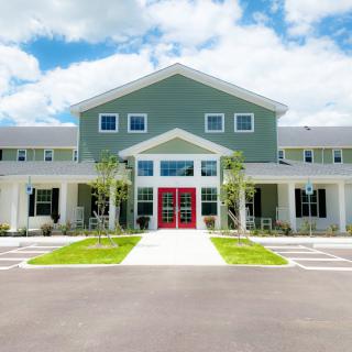 A modern residential building with a symmetrical facade, featuring prominent red doors and surrounded by a clear blue sky.