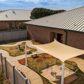 A backyard area with a shade structure, garden, and paved pathways.