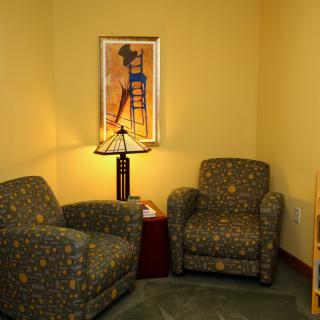 A cozy living room corner with two patterned armchairs, a stylish lamp, and wall artwork.