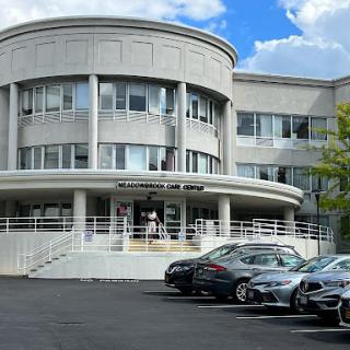 A modern architectural building with a parking lot in front under a blue sky.