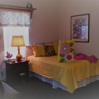 A cozy bedroom with a neatly made bed, colorful cushions, and a warm glowing lamp by the window.