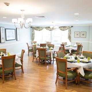 An elegant dining room with neatly arranged tables and chairs, featuring a chandelier and wooden flooring.
