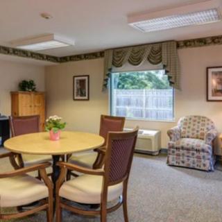 A cozy interior space with a round table, chairs, and an armchair by the window.