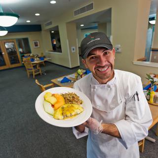 A cheerful chef proudly presents a dish in a restaurant setting.