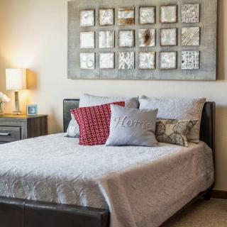 A cozy bedroom with a neatly made bed, decorative pillows, and wall art above the headboard.