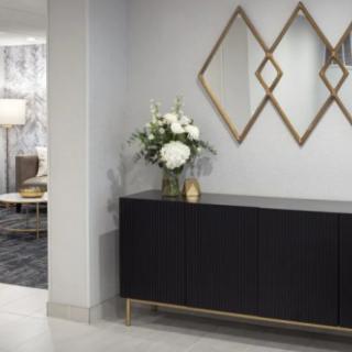 A modern interior with a geometric mirror and black sideboard adorned with a floral arrangement.