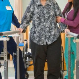 A patient receiving assistance in physical therapy using walking aids.