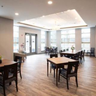 A modern dining room with wooden floors, featuring tables and chairs arranged in a spacious setting.