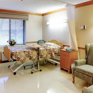 A well-lit hospital patient room featuring two adjustable beds and a seating area.