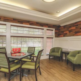 A cozy dining area with green chairs, a wooden floor, and large windows letting in natural light.
