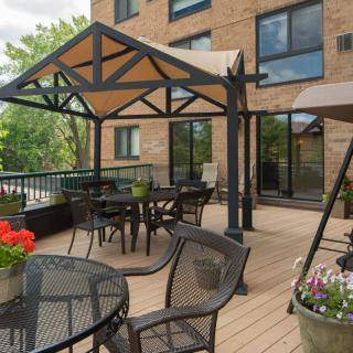 A well-furnished outdoor patio with a gazebo, tables, and chairs on a deck beside a building.