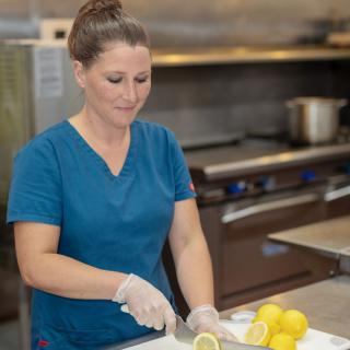 A woman is chopping lemons in a kitchen while wearing gloves.