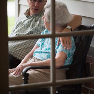 An elderly couple shares a moment of conversation on the porch.