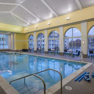 A well-lit indoor swimming pool area featuring large arched windows and seating arrangements.