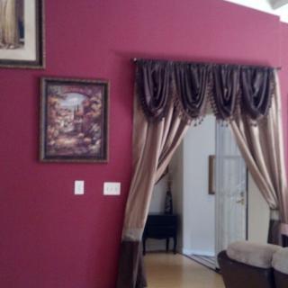 A cozy living room interior with a red accent wall, decorative curtains, and framed artwork.