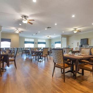 A spacious and well-lit dining area with multiple tables and chairs, featuring ceiling fans and wooden flooring.