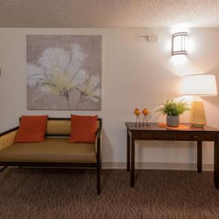 A cozy sitting area featuring a small bench with orange cushions, a decorative table with a lamp and plants, and floral artwork on the wall.