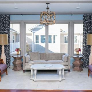 A well-decorated living room with a sofa, coffee table, and chandelier surrounded by large windows.