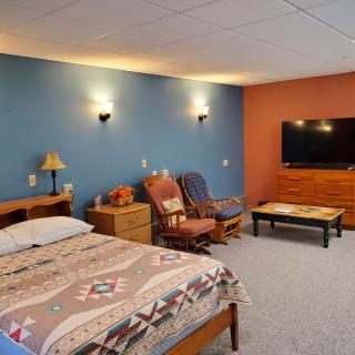 A cozy bedroom with a blue and orange accent wall, featuring a bed, chairs, and a flat-screen TV.