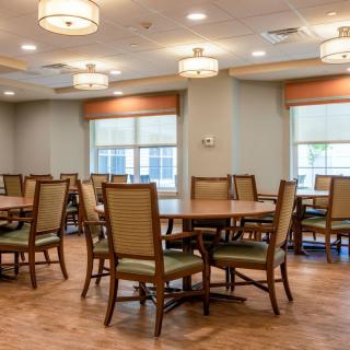 An empty dining room with neatly arranged tables and chairs, illuminated by overhead ceiling lights.