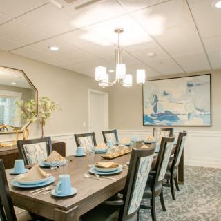 An elegantly decorated dining room with a large rectangular table set for eight, featuring modern decor and a stylish chandelier.
