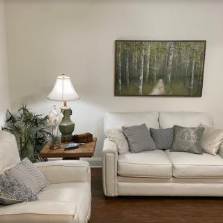 A cozy living room with white sofas, a side table with a lamp, and artwork on the wall.