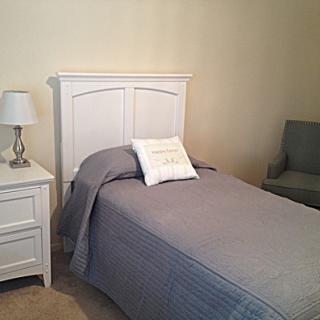 A cozy bedroom with a single bed, gray bedding, and a white nightstand with a lamp.