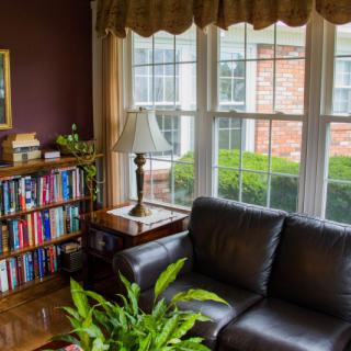 A cozy living room with a leather sofa, bookshelf, and large windows letting in natural light.