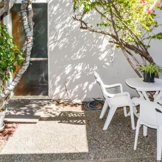 A sunny patio with white plastic chairs and a table surrounded by plants.