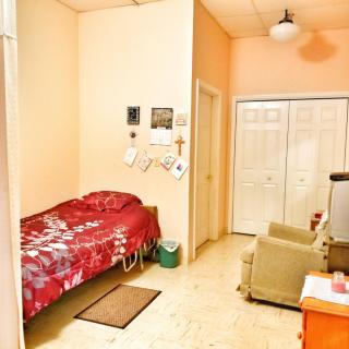 A cozy bedroom with a single bed, armchair, television, and wardrobe.