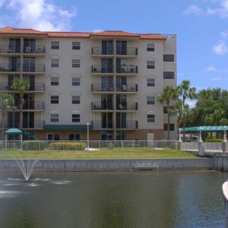 A residential apartment building next to a pond with a fountain and surrounded by palm trees.
