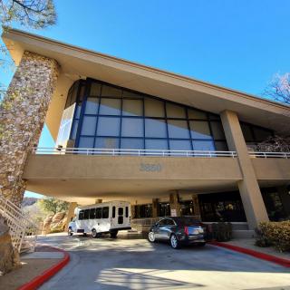 A modern building entrance with large glass windows and vehicles parked in front.