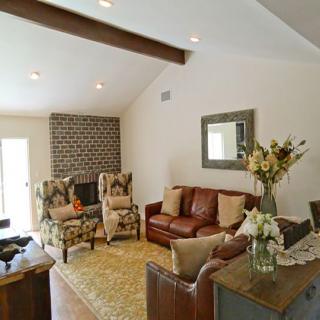 A cozy living room featuring a brick fireplace, leather sofa, patterned armchairs, and a coffee table adorned with a vase of flowers.