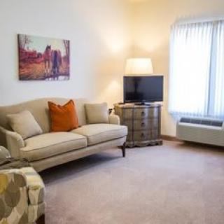 A cozy living room with a sofa, artwork on the wall, and a television beside a window.