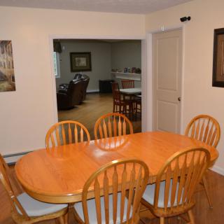 A dining room with a wooden table and six chairs, leading to a view of the living area.