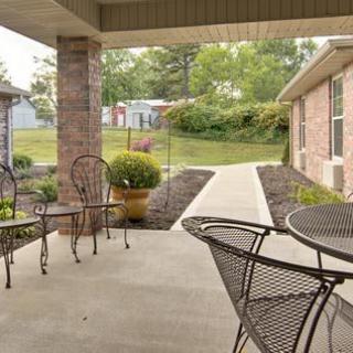A cozy patio with metal chairs and a table, overlooking a landscaped walkway.