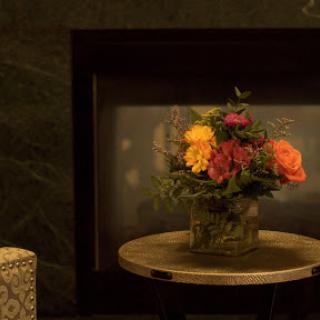 A beautiful floral arrangement sits on a wooden table, illuminated by the warm glow of a nearby fireplace.