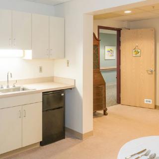 A small kitchen area with a sink, cabinets, and a doorway leading to another room.
