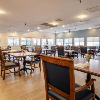 An empty dining room with wooden tables and chairs, softly lit by overhead lights.