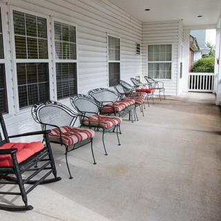 A porch with several chairs and a rocking chair, featuring outdoor seating arrangements.