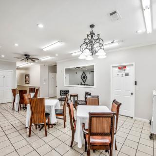 A well-lit dining area with multiple tables and chairs, featuring a chandelier and tiled flooring.