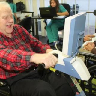 An elderly person engaging in physical therapy using exercise equipment in a healthcare setting.
