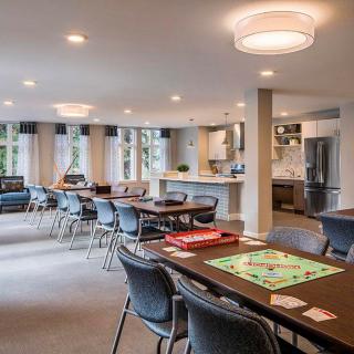 A spacious community room featuring game tables, comfortable seating, and a modern kitchen.