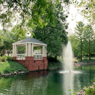 A serene park scene featuring a gazebo beside a fountain, surrounded by lush greenery.